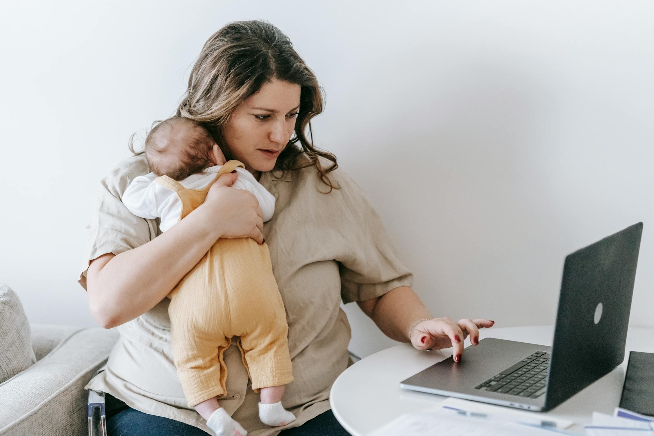 Mother holding baby while working on laptop